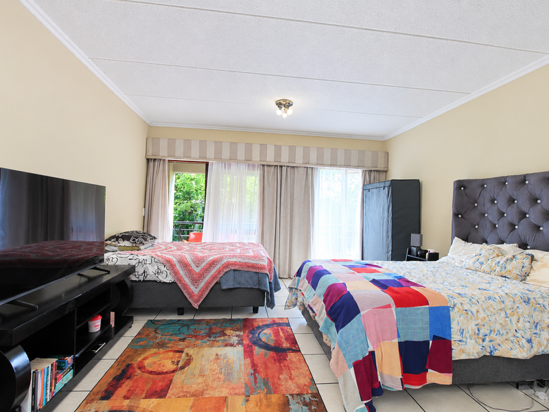 Spacious bedroom featuring tiled flooring, neutral wall tones, and direct access to a private balcony through sliding glass doors.