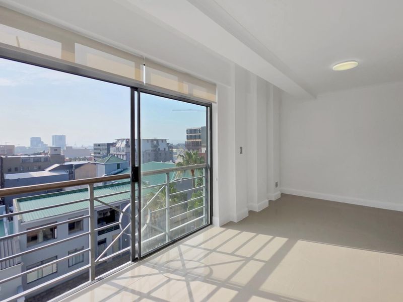 Bright and spacious living area featuring large sliding glass doors that open to a balcony with expansive city views.