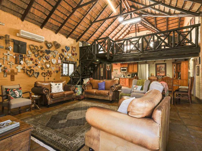 Spacious open-plan living area featuring a high exposed thatch roof, mezzanine level, timber staircase, and rustic terracotta flooring.