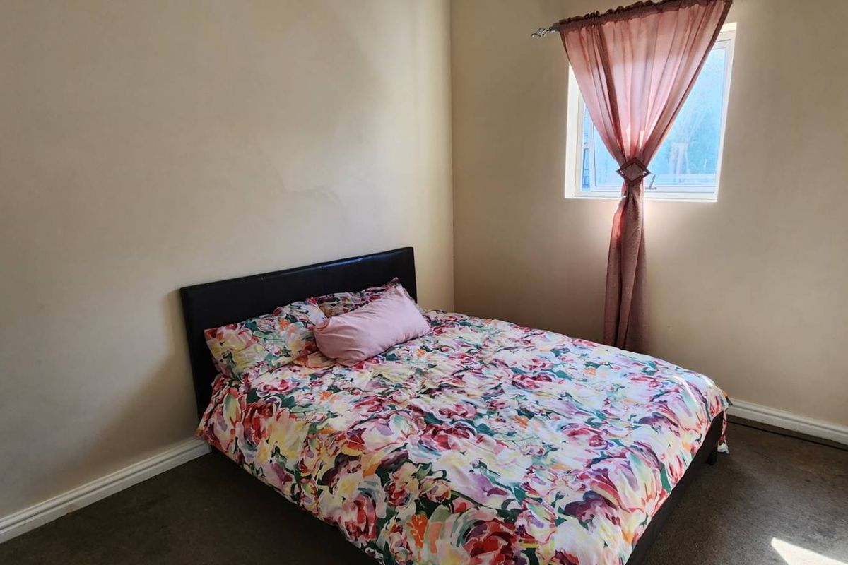 A compact bedroom featuring neutral walls, a single window with curtain, and carpeted flooring.