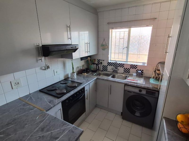 Compact kitchen featuring grey cabinetry, marble-look laminate countertops, built-in oven and hob, and a double basin sink with tiled backsplash.