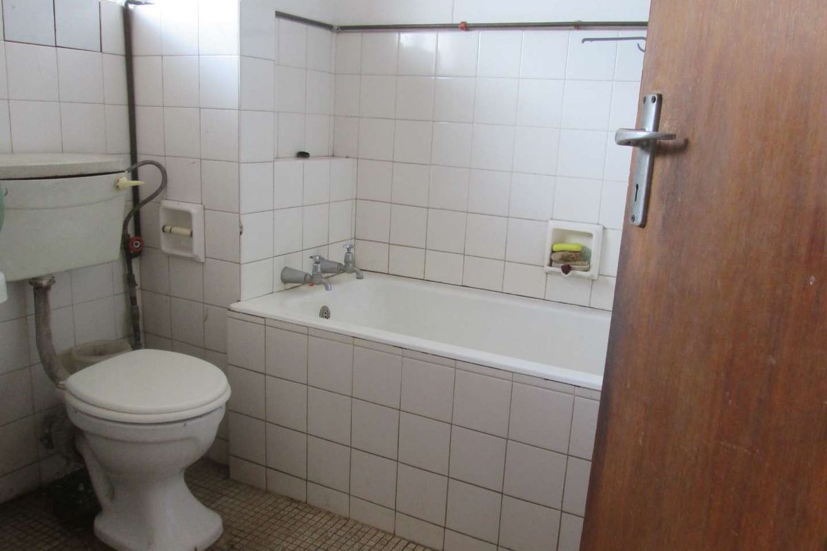 A dated bathroom featuring a standard bathtub, toilet, and tiled finishes, requiring modernization to improve its overall aesthetic and functionality.