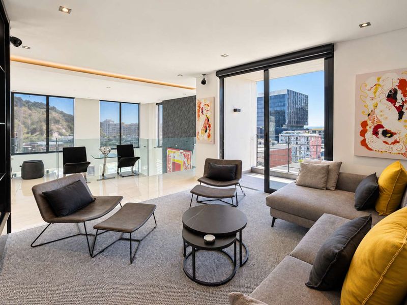 Spacious open-plan living area featuring modern recessed lighting, sleek tiled and carpeted flooring, and large sliding glass doors leading to a balcony with city views.