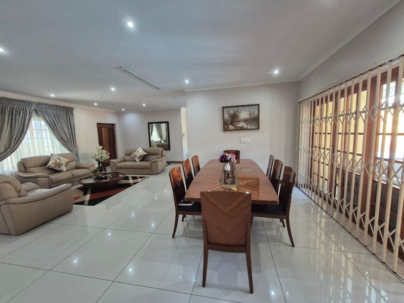 Spacious open-plan living and dining area featuring polished porcelain floor tiles, recessed downlighting, and large sliding doors with integrated security gates.