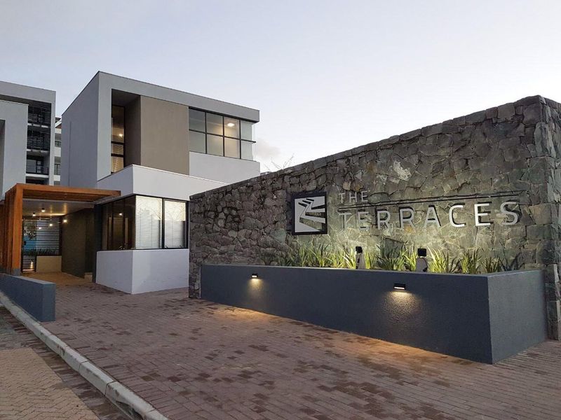 The entrance facade of The Terraces apartment complex, featuring a stone-clad feature wall, modern architectural design, and paved driveway.