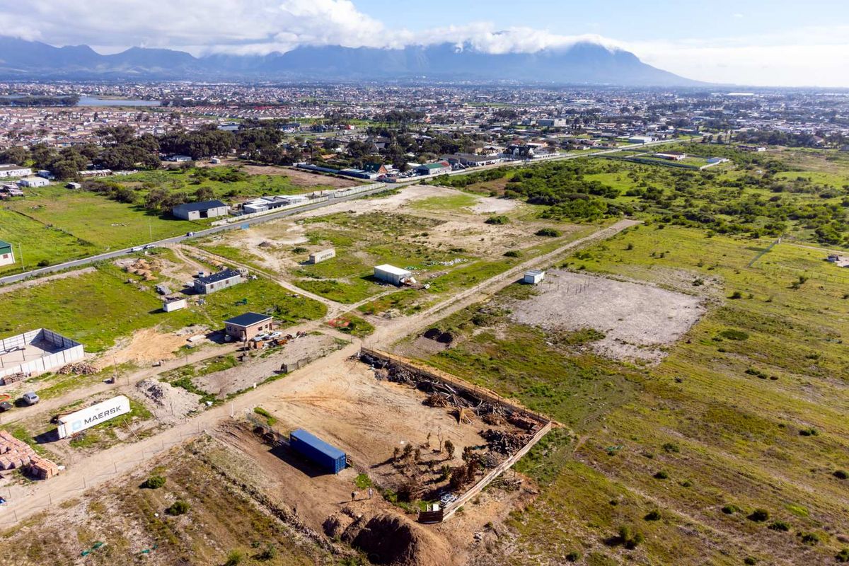 Aerial view of a large vacant agricultural land plot with surrounding infrastructure and mountain views in the distance.