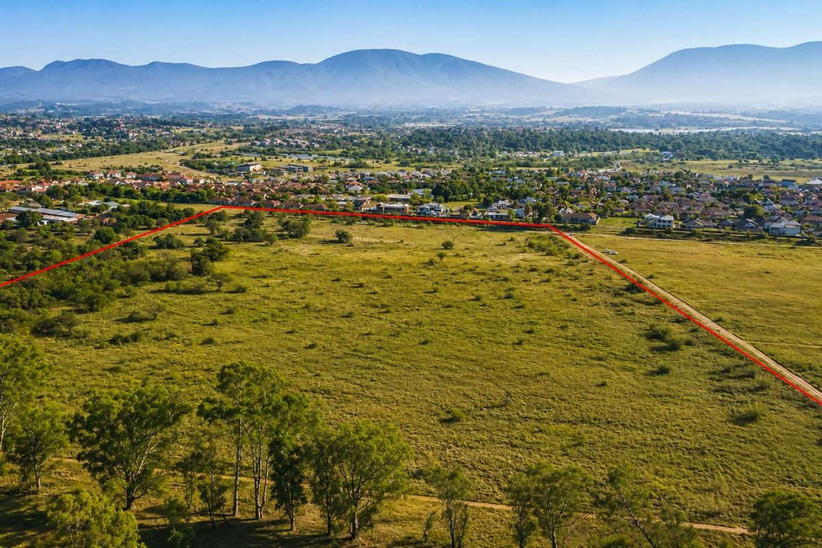 An aerial view of a large, undeveloped farm plot with clear boundary markings, set against a scenic mountain landscape.
