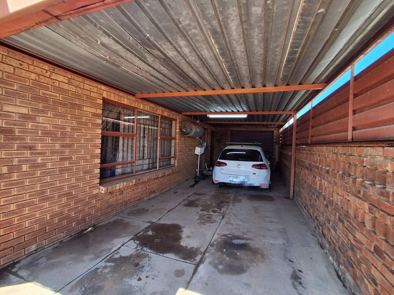 A covered carport or garage area featuring brick walls, a corrugated metal roof, and a concrete floor with visible surface staining.