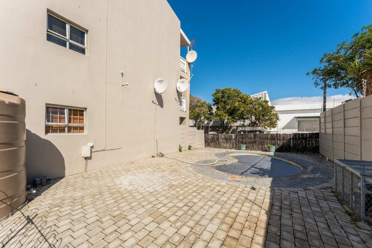 Rear exterior view of the apartment building featuring a paved courtyard area and a swimming pool with a safety cover.