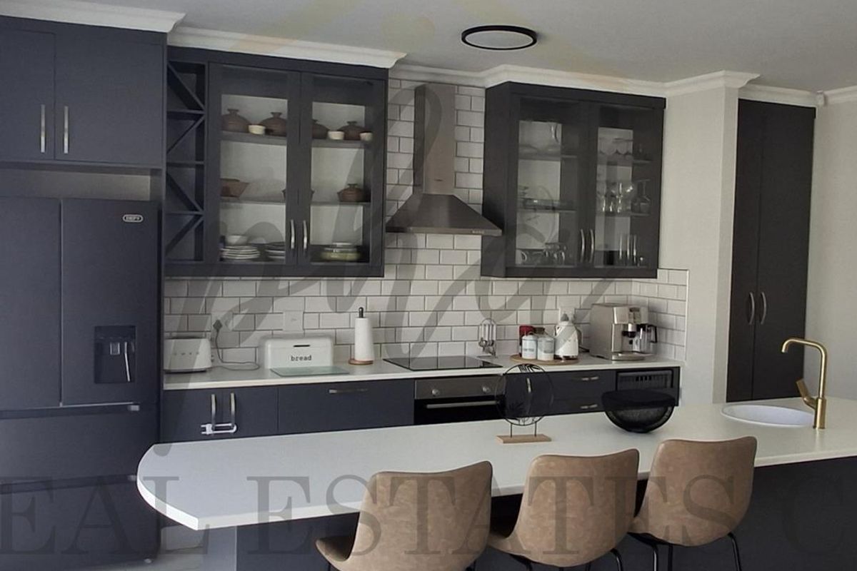 Modern kitchen featuring dark cabinetry, white quartz countertops, subway tile backsplash, integrated appliances, and a central island with breakfast bar seating.