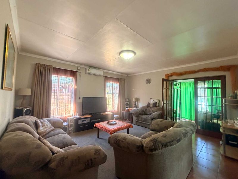 A spacious living room featuring split-system air conditioning, tiled and carpeted flooring, and classic french doors leading to an adjacent area.