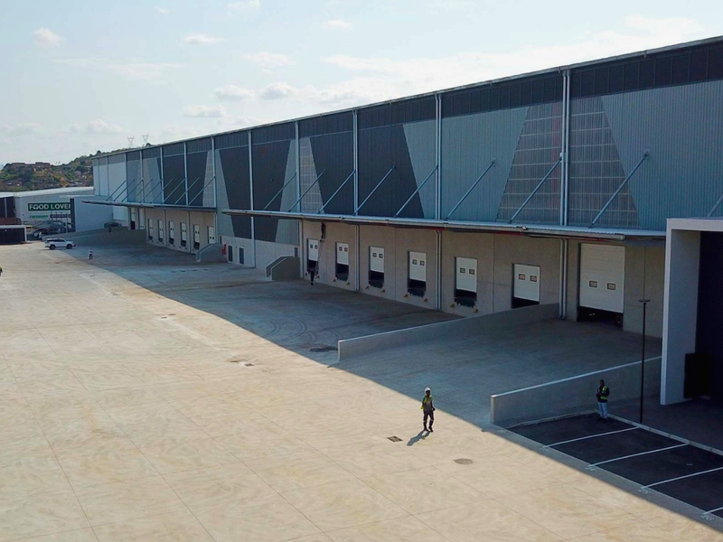 Aerial view of a modern industrial warehouse featuring multiple loading docks, roller shutter doors, and a spacious concrete yard for logistics operations.