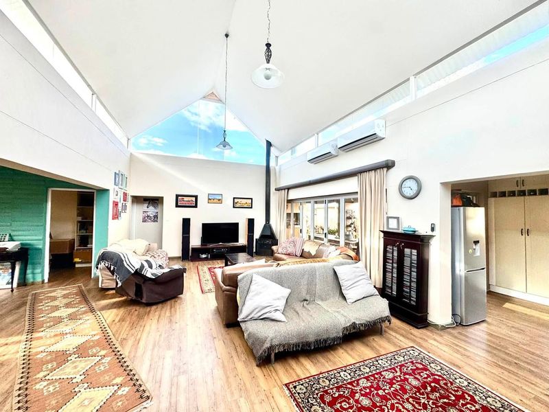 Spacious open-plan living area featuring a dramatic vaulted ceiling, clerestory windows for natural light, a wood-burning fireplace, and split-system air conditioning.