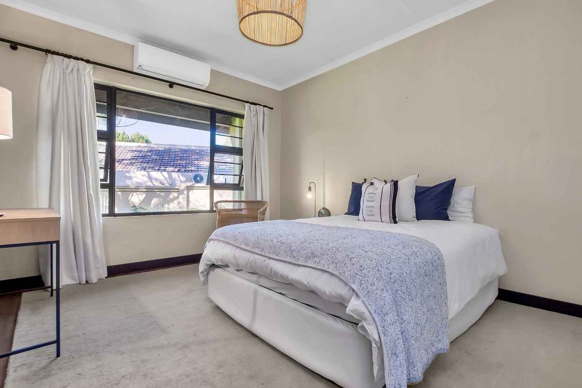 A well-lit bedroom featuring neutral walls, carpeted flooring, and a wall-mounted air conditioning unit.