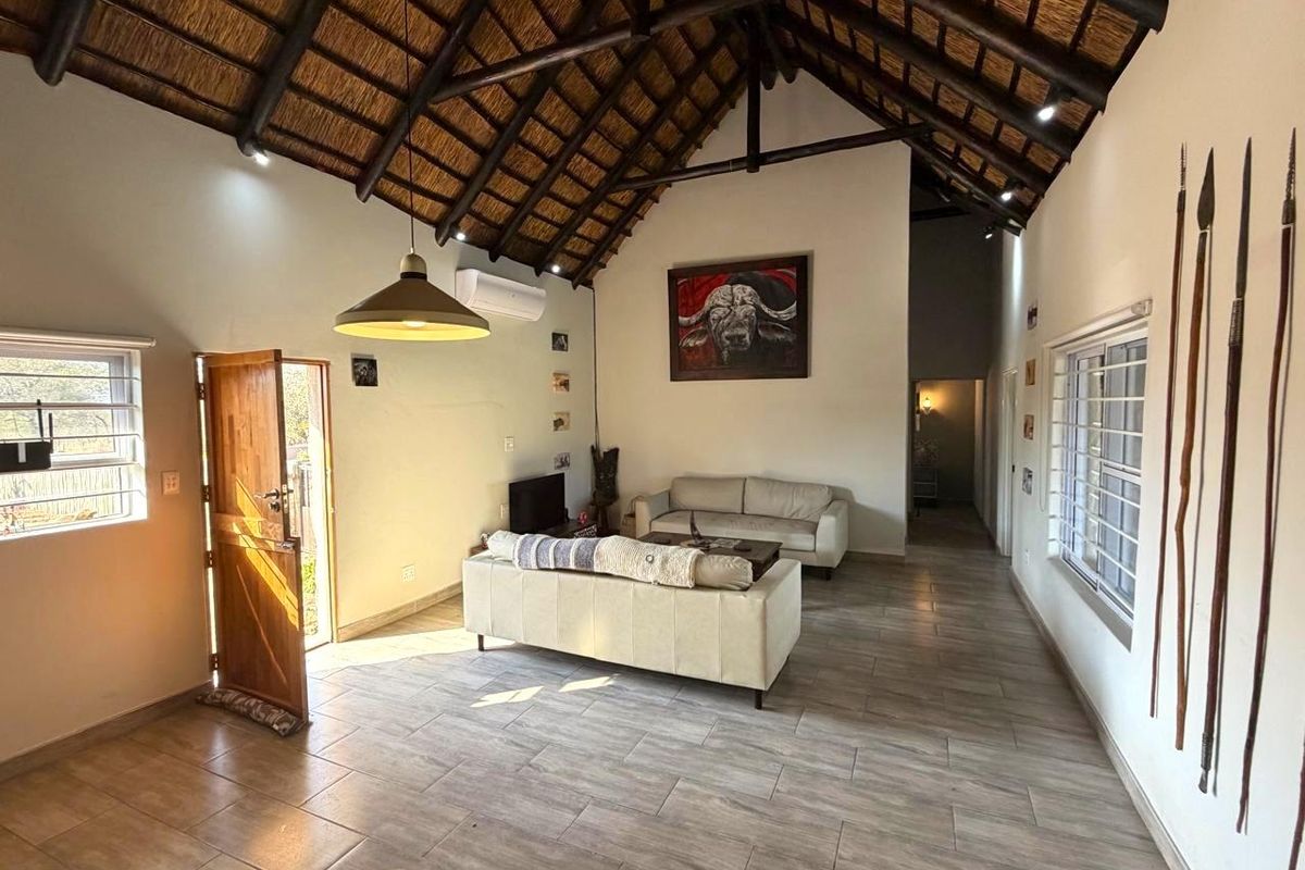 Spacious living area featuring a high vaulted thatched ceiling with exposed timber trusses, tiled flooring, and a wall-mounted air conditioning unit.