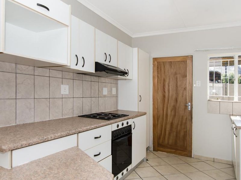A functional kitchen featuring white cabinetry, laminate countertops, built-in oven and hob, tiled backsplash, and direct access to the exterior.