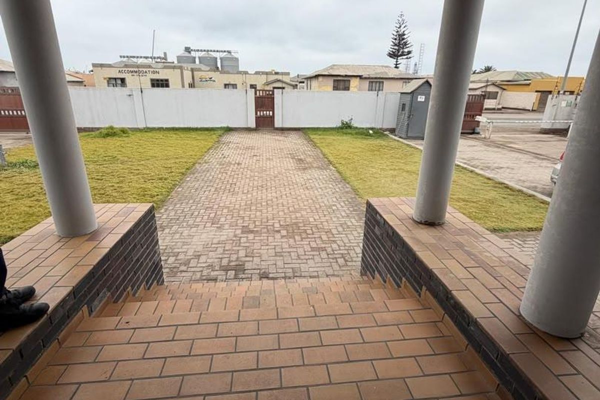 View from a covered porch overlooking a paved driveway, lawn, and perimeter wall in an office property setting.