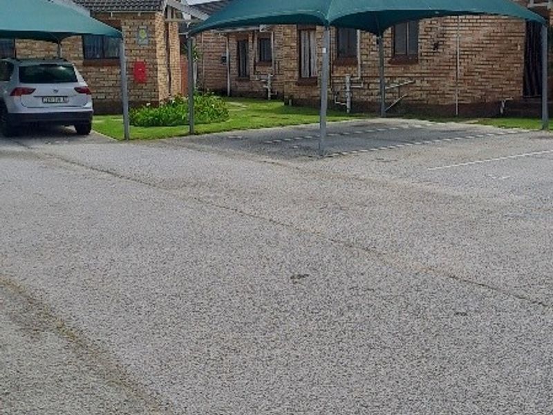 Exterior view of a townhouse complex featuring face brick facades, tiled roofs, and dedicated shade cloth parking bays for residents.