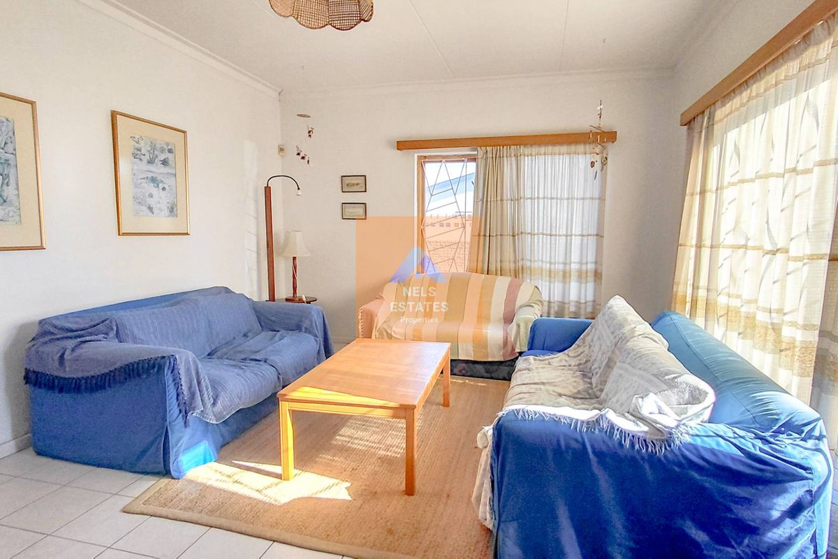 A bright living room featuring tiled flooring and large windows with security gates, offering a comfortable and functional space for relaxation.