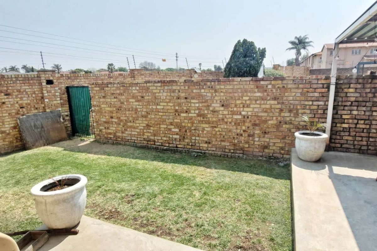 A private rear garden featuring a paved patio area, a small lawn, and high perimeter brick boundary walls with security fencing.