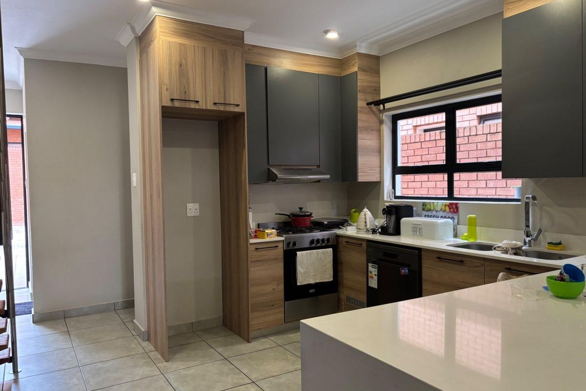 Modern kitchen featuring two-tone cabinetry, stone countertops, integrated stove with extractor fan, and tiled flooring, offering a functional and contemporary cooking space.