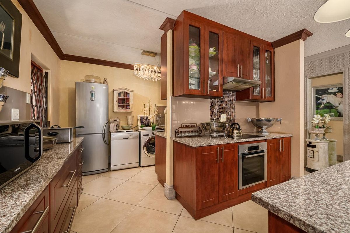 A functional kitchen featuring dark wood cabinetry, granite countertops, a mosaic tile backsplash, and integrated stainless steel oven and extractor fan.