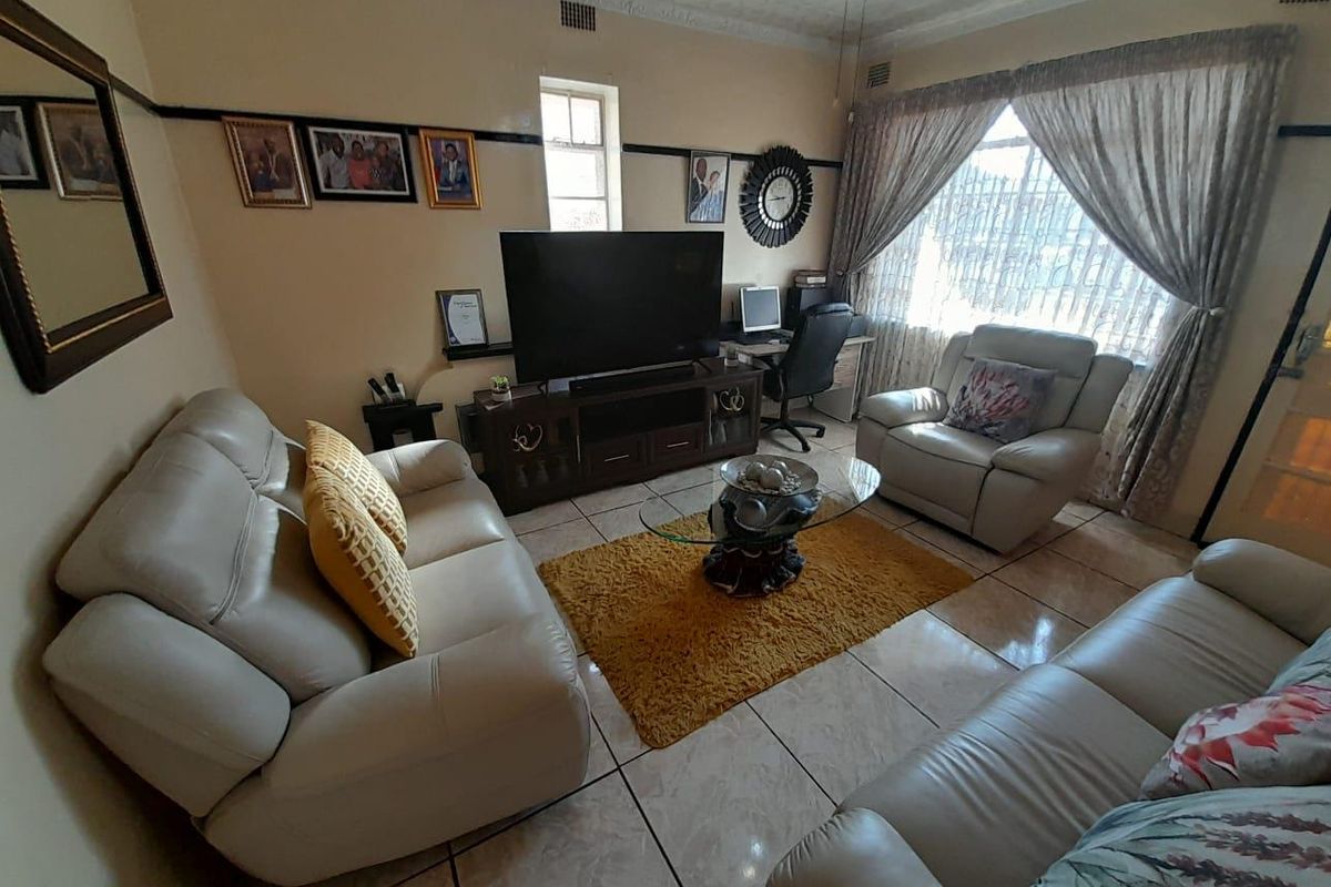 A comfortable living room featuring tiled flooring, decorative ceiling cornices, and a large window with curtains, providing a functional space for relaxation.