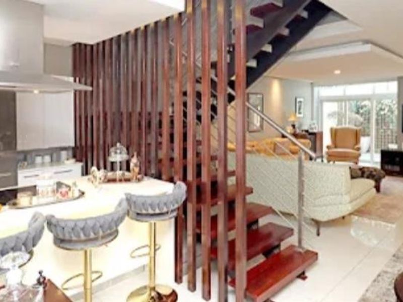 An open-plan living area featuring a modern kitchen with a central island, stainless steel extractor, and a striking timber staircase with a slatted screen divider.