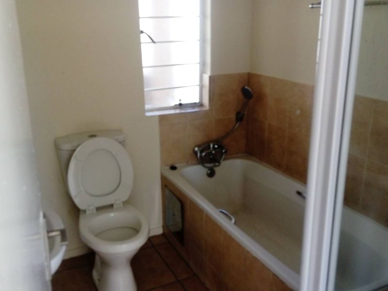 A functional bathroom featuring a standard bathtub with shower mixer, toilet, and tiled finishes, offering a clean and practical layout.