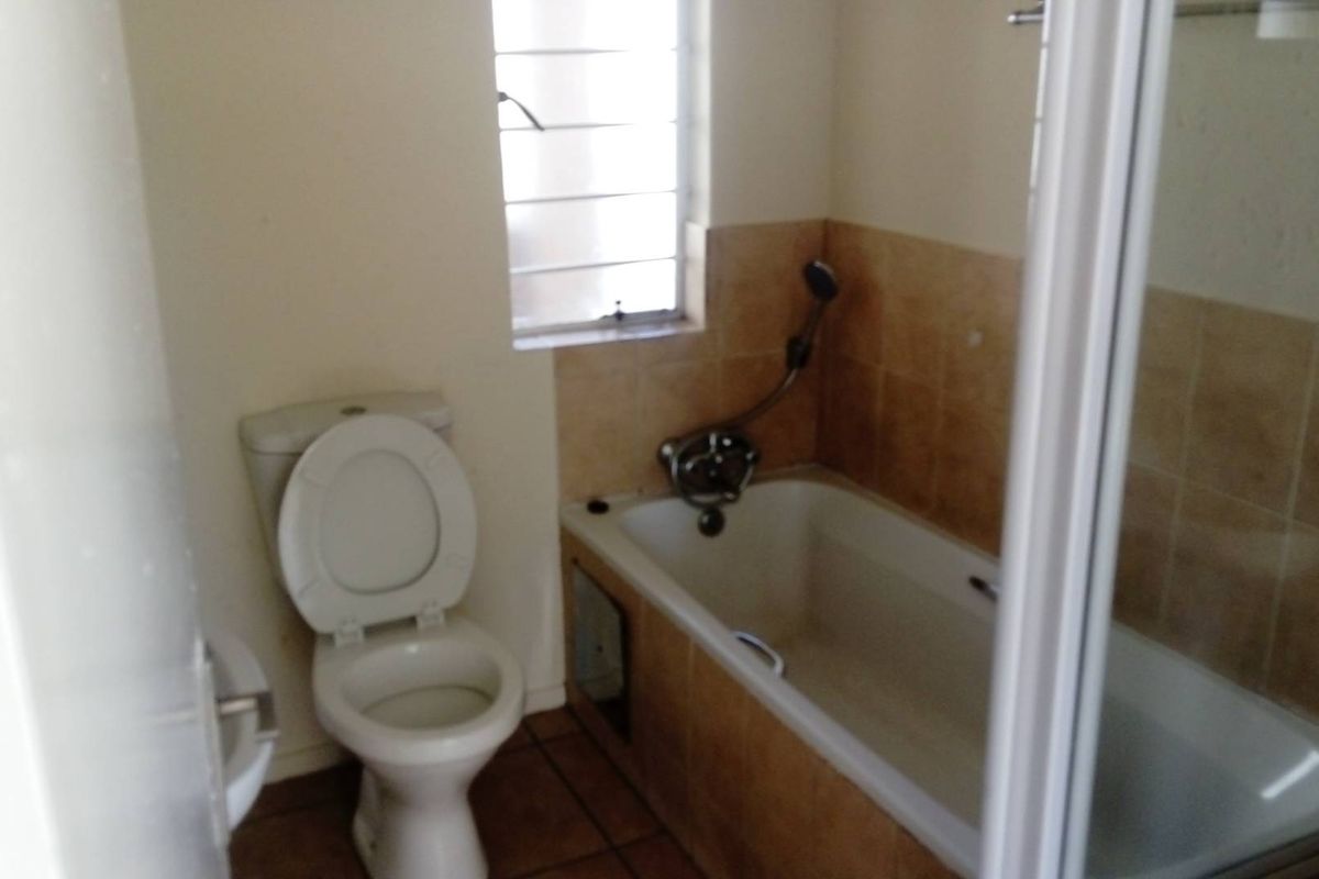 A functional bathroom featuring a standard bathtub with shower mixer, toilet, and tiled finishes, offering a clean and practical layout.