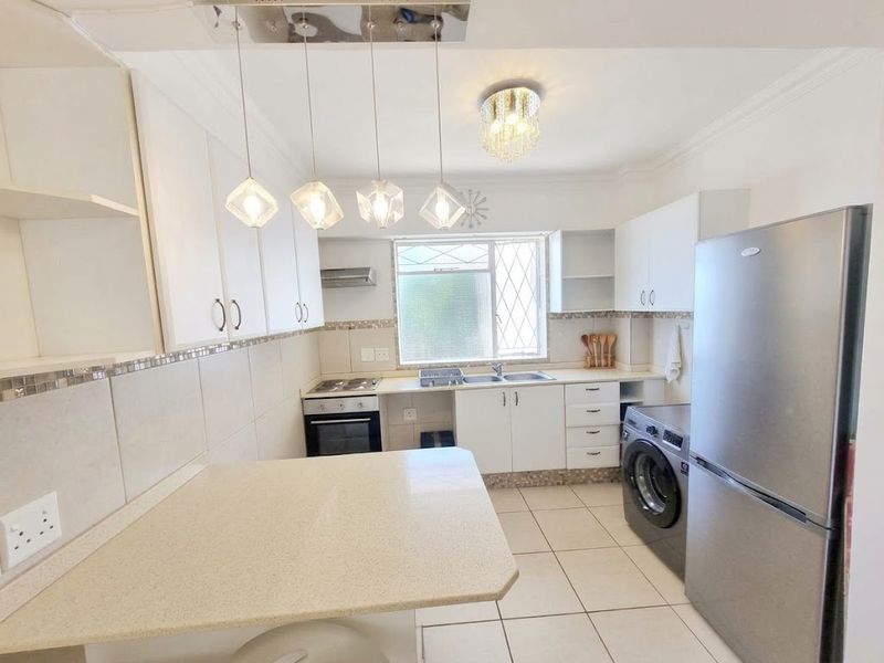 A functional kitchen featuring white cabinetry, stone countertops, a breakfast nook, and integrated appliances, complemented by tiled flooring and a tiled backsplash.