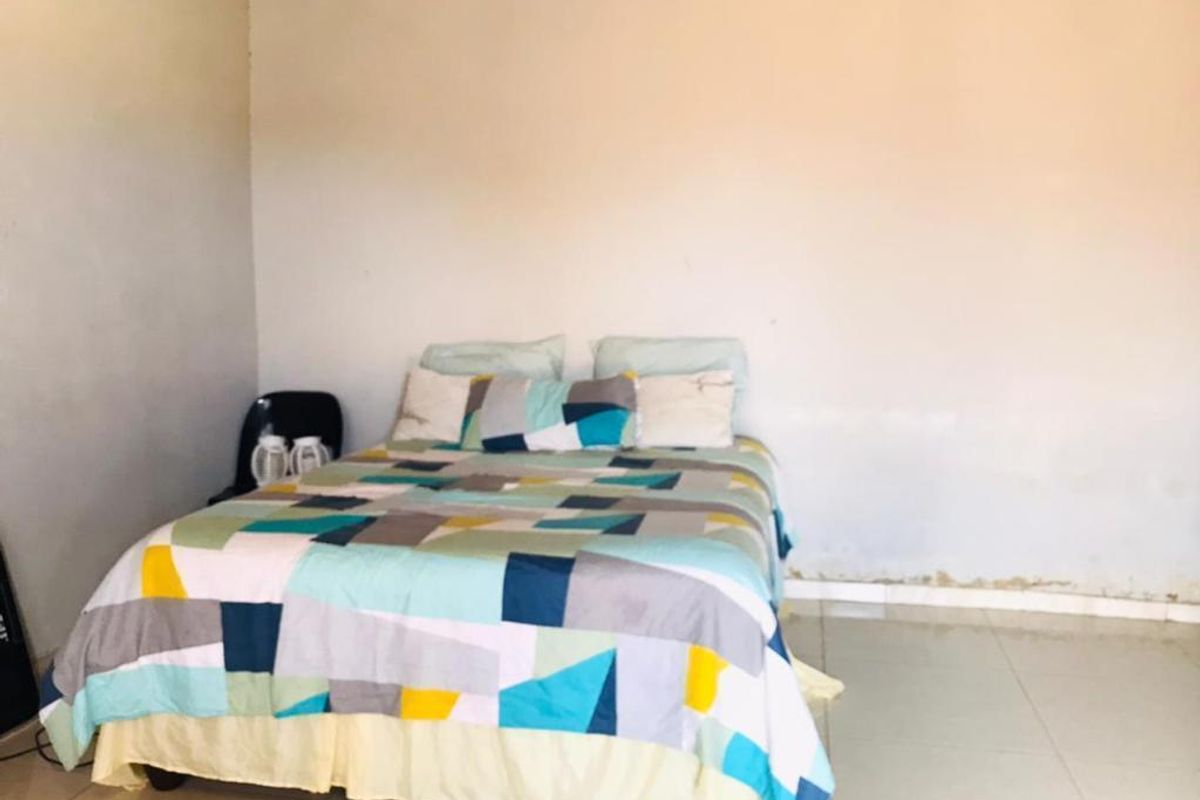 A bedroom featuring tiled flooring and plain walls, showing signs of wear near the baseboards.