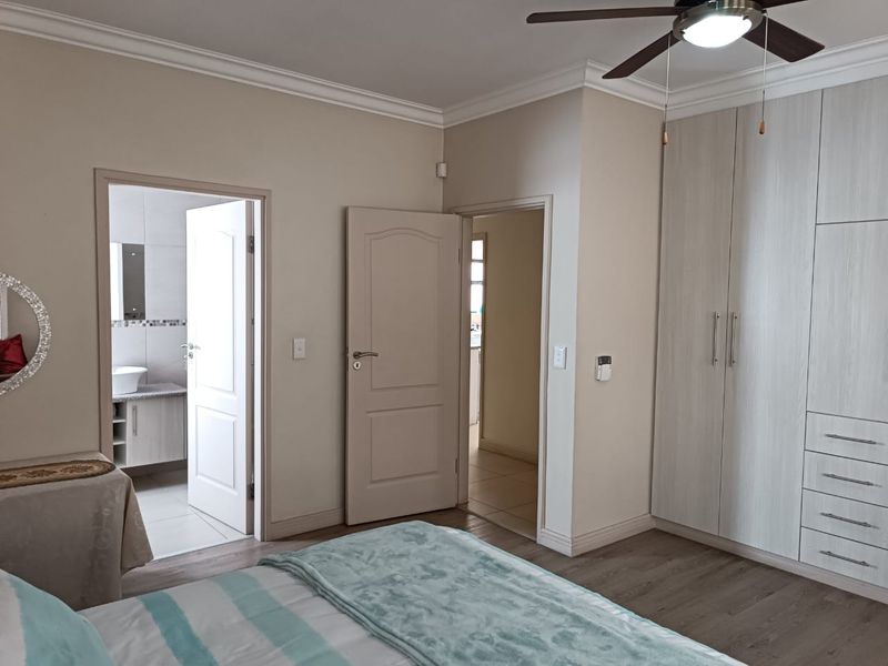 A well-maintained bedroom featuring laminate flooring, built-in cupboards, a ceiling fan, and direct access to an en-suite bathroom.