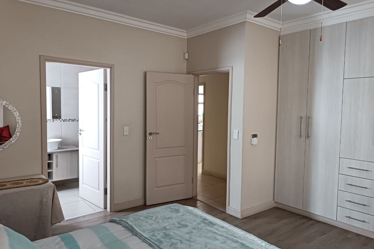 A well-maintained bedroom featuring laminate flooring, built-in cupboards, a ceiling fan, and direct access to an en-suite bathroom.