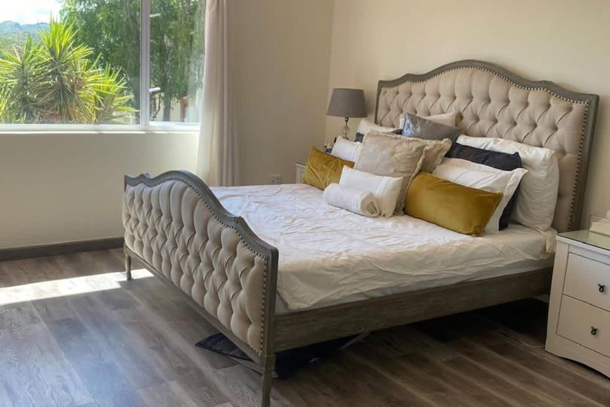 A well-maintained bedroom featuring modern laminate flooring, a split-system air conditioner, and a decorative crystal chandelier, offering a bright and comfortable living space.