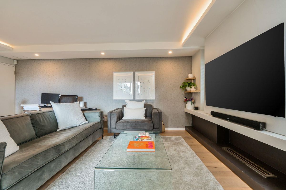 A modern, well-maintained living room featuring timber flooring, recessed ceiling lighting, and a sleek built-in media console.