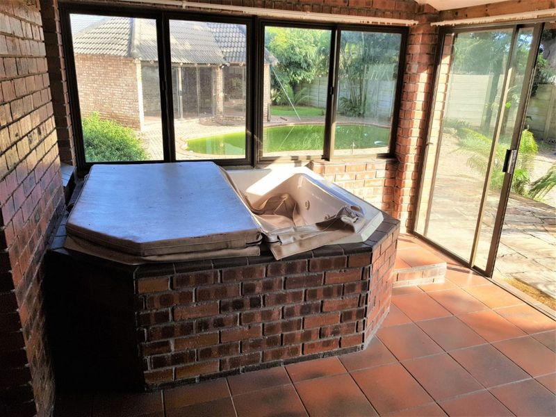 Enclosed patio area featuring a built-in spa bath, brick walls, and tiled flooring with direct views of the garden and swimming pool.