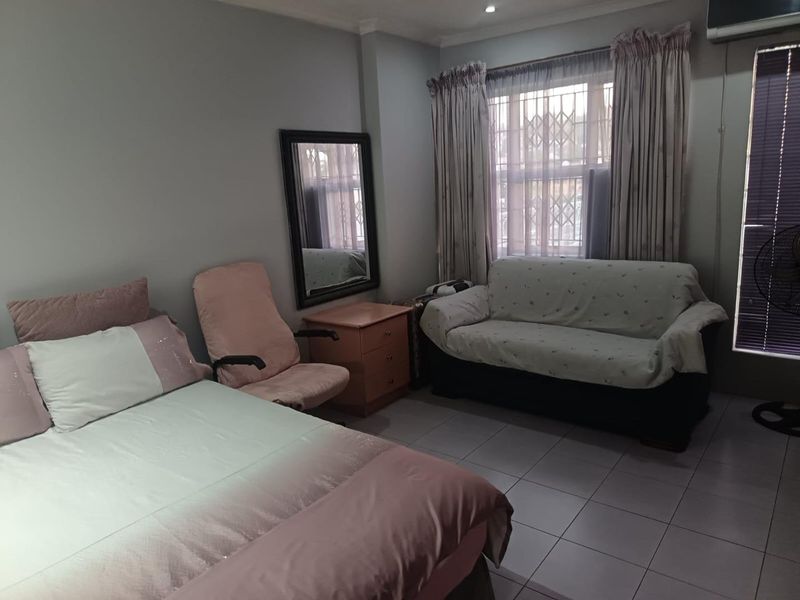 A functional bedroom featuring tiled flooring, security bars on the windows, and an integrated air conditioning unit.