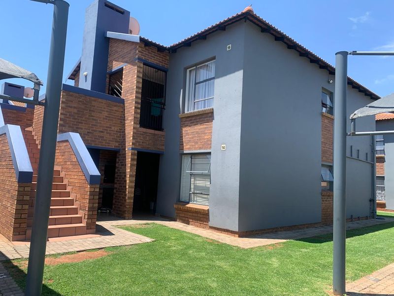 Exterior view of a multi-story townhouse unit featuring a brick and painted facade, external staircase, and surrounding landscaped garden area.
