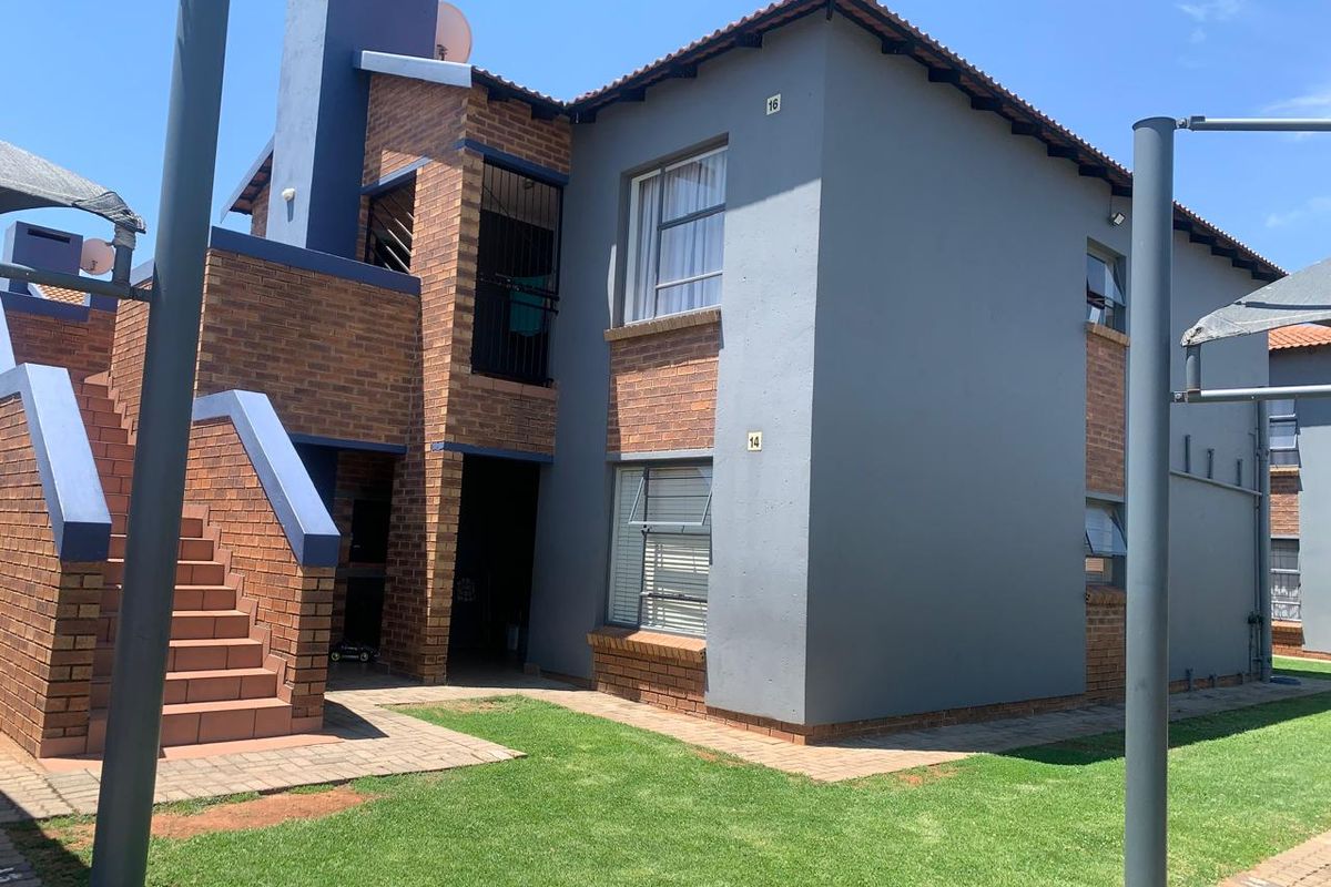 Exterior view of a multi-story townhouse unit featuring a brick and painted facade, external staircase, and surrounding landscaped garden area.