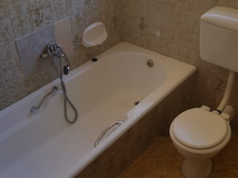 A dated bathroom featuring a standard bathtub with shower mixer, toilet, and original wall tiling, offering potential for a modern renovation.