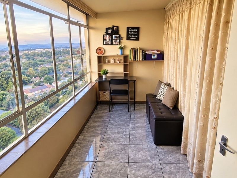 Enclosed balcony featuring tiled flooring and expansive windows offering panoramic views, suitable as a sunroom or home office space.