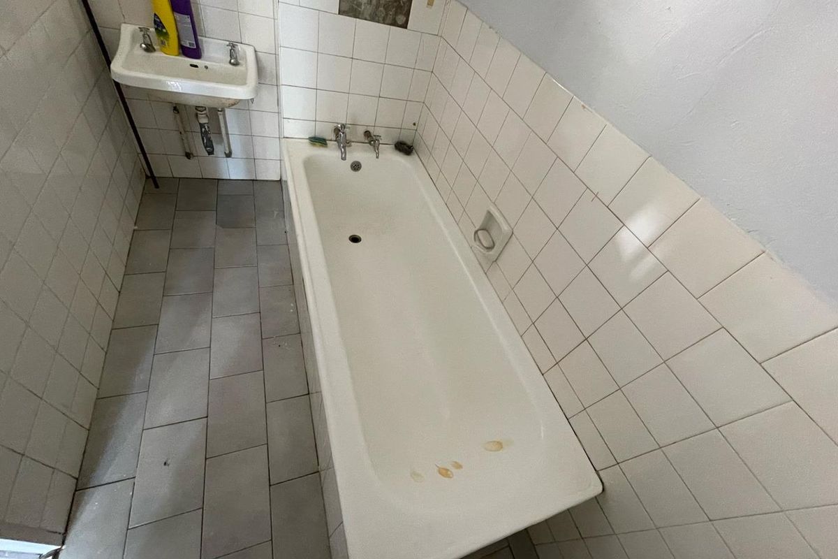 A dated bathroom featuring a standard bathtub, wall-mounted basin, and tiled walls requiring maintenance and cosmetic updates.