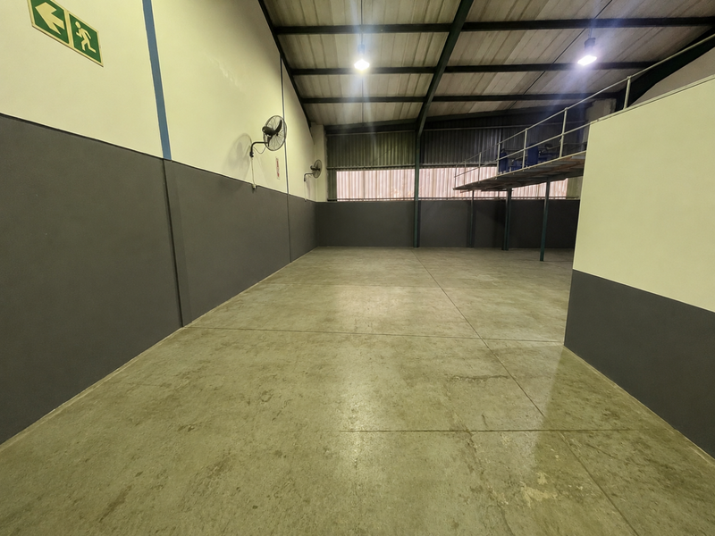 A spacious, empty industrial utility area featuring polished concrete floors, exposed steel roof trusses, and a mezzanine level, suitable for storage or workshop use.
