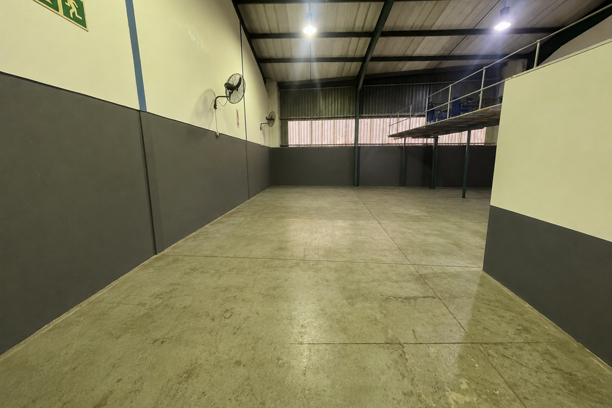 A spacious, empty industrial utility area featuring polished concrete floors, exposed steel roof trusses, and a mezzanine level, suitable for storage or workshop use.