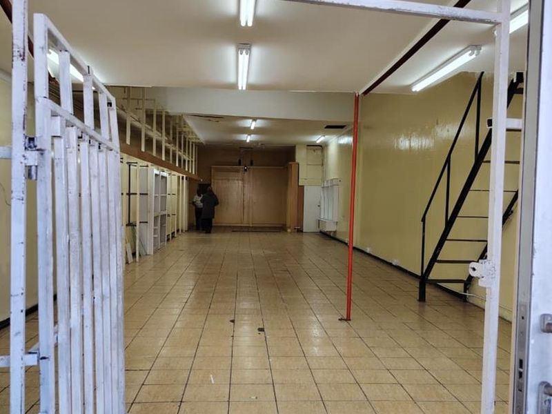 An empty commercial utility or retail space featuring tiled flooring, fluorescent lighting, built-in shelving, and a metal staircase leading to an upper level.