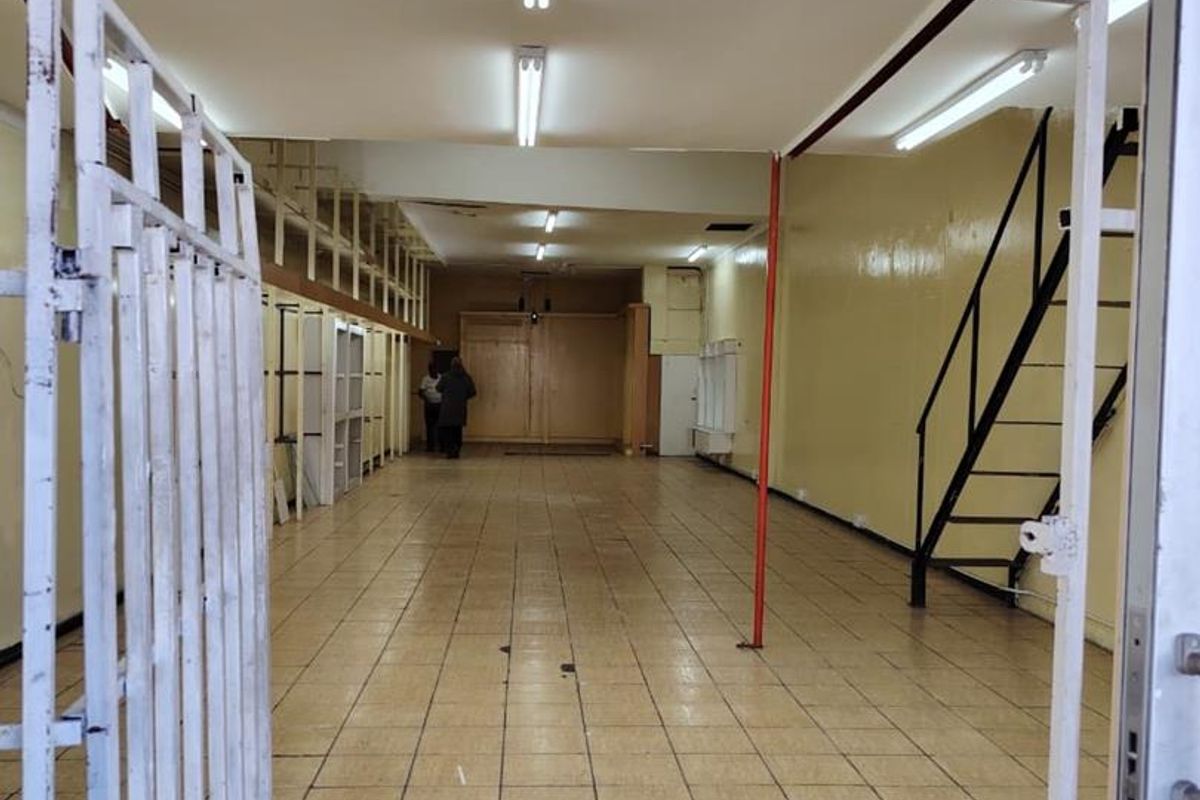 An empty commercial utility or retail space featuring tiled flooring, fluorescent lighting, built-in shelving, and a metal staircase leading to an upper level.