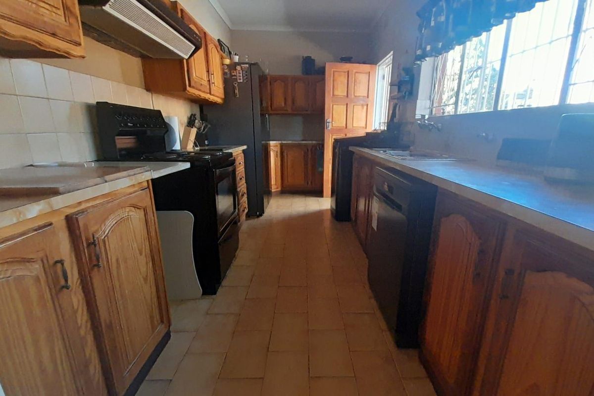 A functional kitchen featuring wooden cabinetry, tiled flooring, a tiled backsplash, and a built-in extractor fan with security bars on the windows.