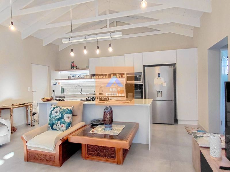 Modern open-plan living area featuring a contemporary kitchen with island, subway tile backsplash, and high vaulted ceilings with exposed white timber trusses.