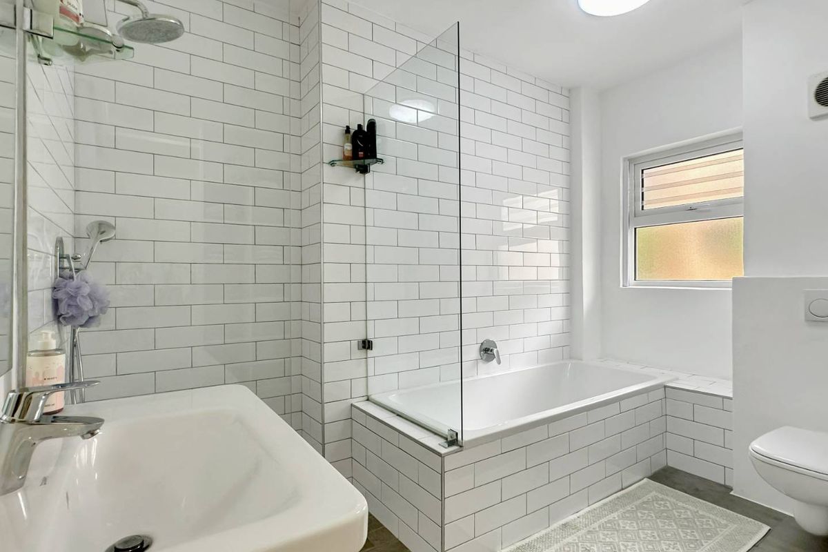 Modern bathroom featuring white subway tile wall cladding, a built-in bathtub with a glass screen, a wall-mounted toilet, and a clean basin.